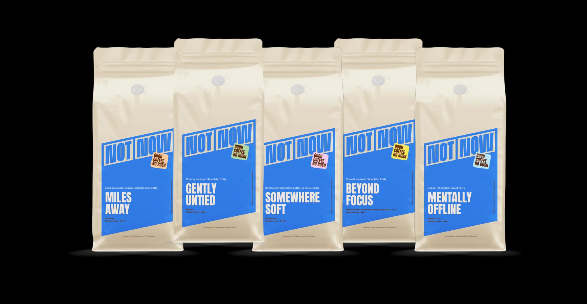 Vijf crèmekleurige zakken koffiebonen van Not Now met blauwe etiketten, naast elkaar tegen een zwarte achtergrond.